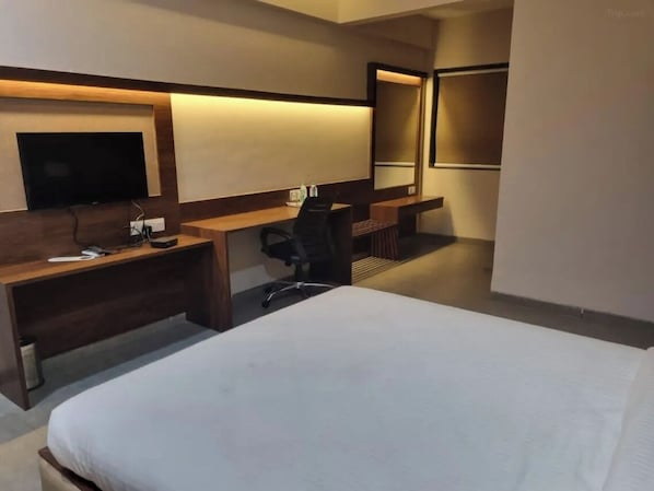 A hotel room with a bed, a desk, a chair, a TV, and a mirror. - Club Azzurro Resort - Nalsarovar (Bavla)