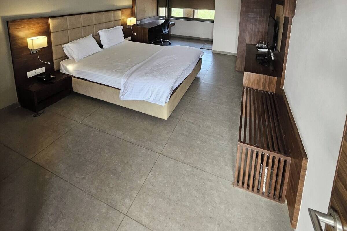 A modern hotel room with a large bed, a ceiling fan, an air conditioning unit, a TV, and a small desk area.