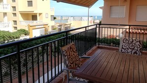 A balcony with a wooden table and chairs, a striped awning, and a view of the sea and buildings. - Oasis  1º Solo Familias! (Xeraco Playa)