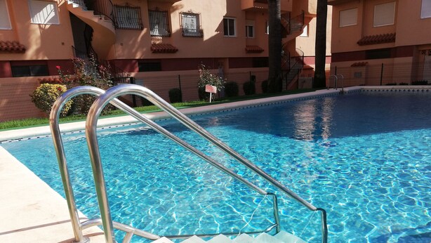 A swimming pool with a metal ladder and steps leading into the water. - Oasis  1º Solo Familias! (Xeraco Playa)