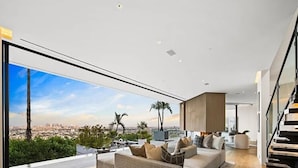 Een moderne woonkamer met een groot raam, een bank en een trap.