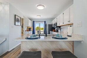 Une cuisine moderne avec des meubles blancs, un îlot central et une vue sur l’extérieur.