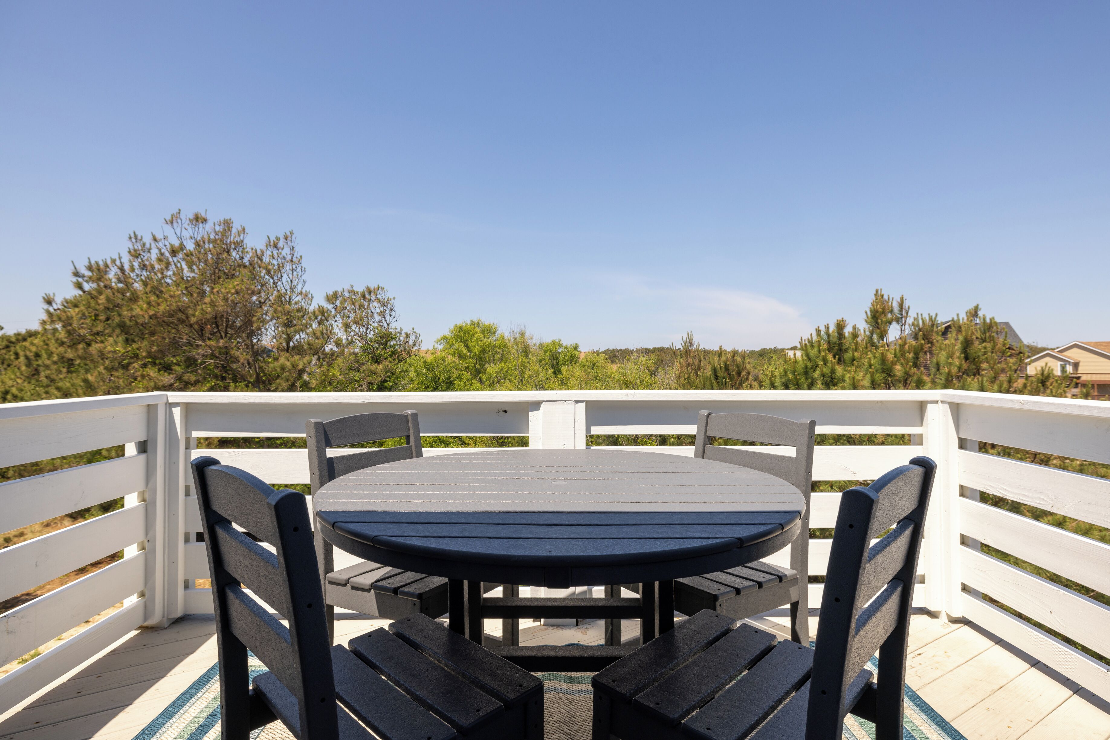 Una mesa redonda con cuatro sillas sobre una terraza con barandas blancas, rodeada de follaje.