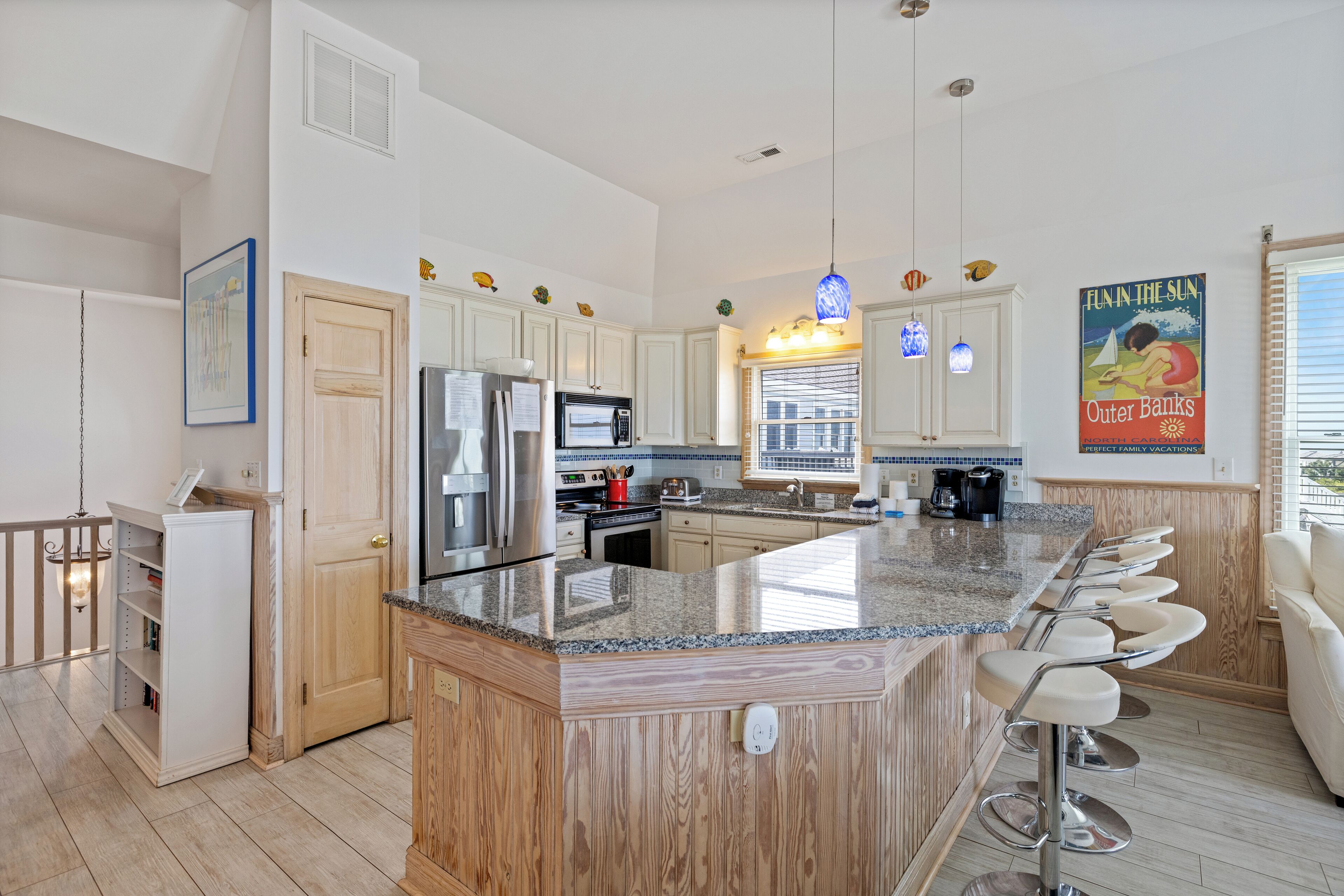 A modern kitchen with a central island, bar stools, and a large window.