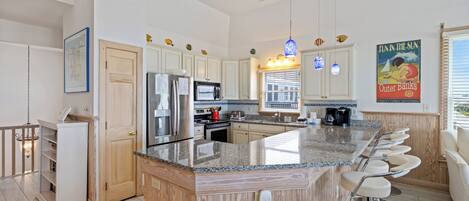 A modern kitchen with a central island, bar stools, and a large window.