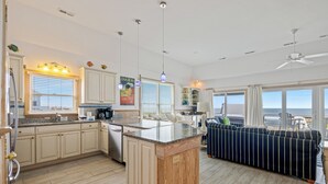 A spacious kitchen with a central island, a dining area with a sofa, and large windows offering a view of the ocean. - Direct Oceanfront Access*Hot Tub*Neighborhood Pool (Nags Head)