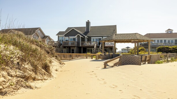 A beachfront property with a large house, a covered patio, and a sandy beach. - Direct Oceanfront Access*Hot Tub*Neighborhood Pool (Nags Head)