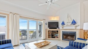 A living room with a TV, fireplace, and a view of the ocean. - Direct Oceanfront Access*Hot Tub*Neighborhood Pool (Nags Head)