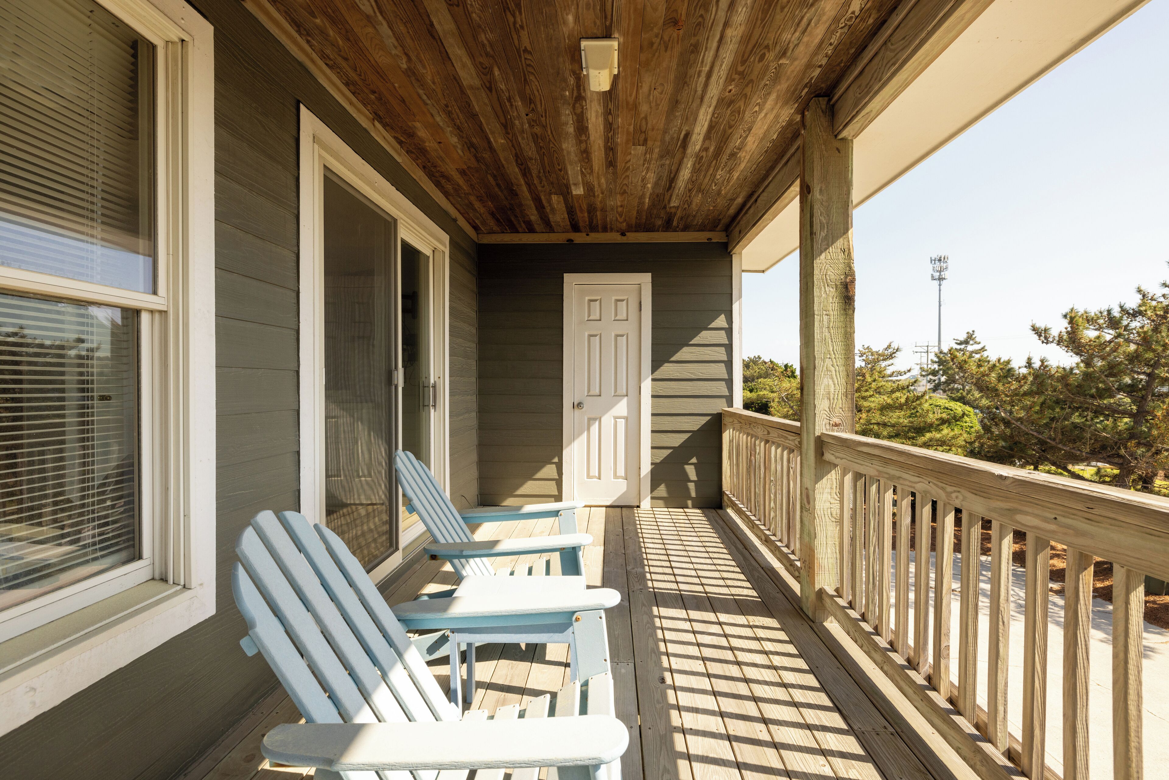 A wooden porch with two Adirondack chairs, a door, and a railing.