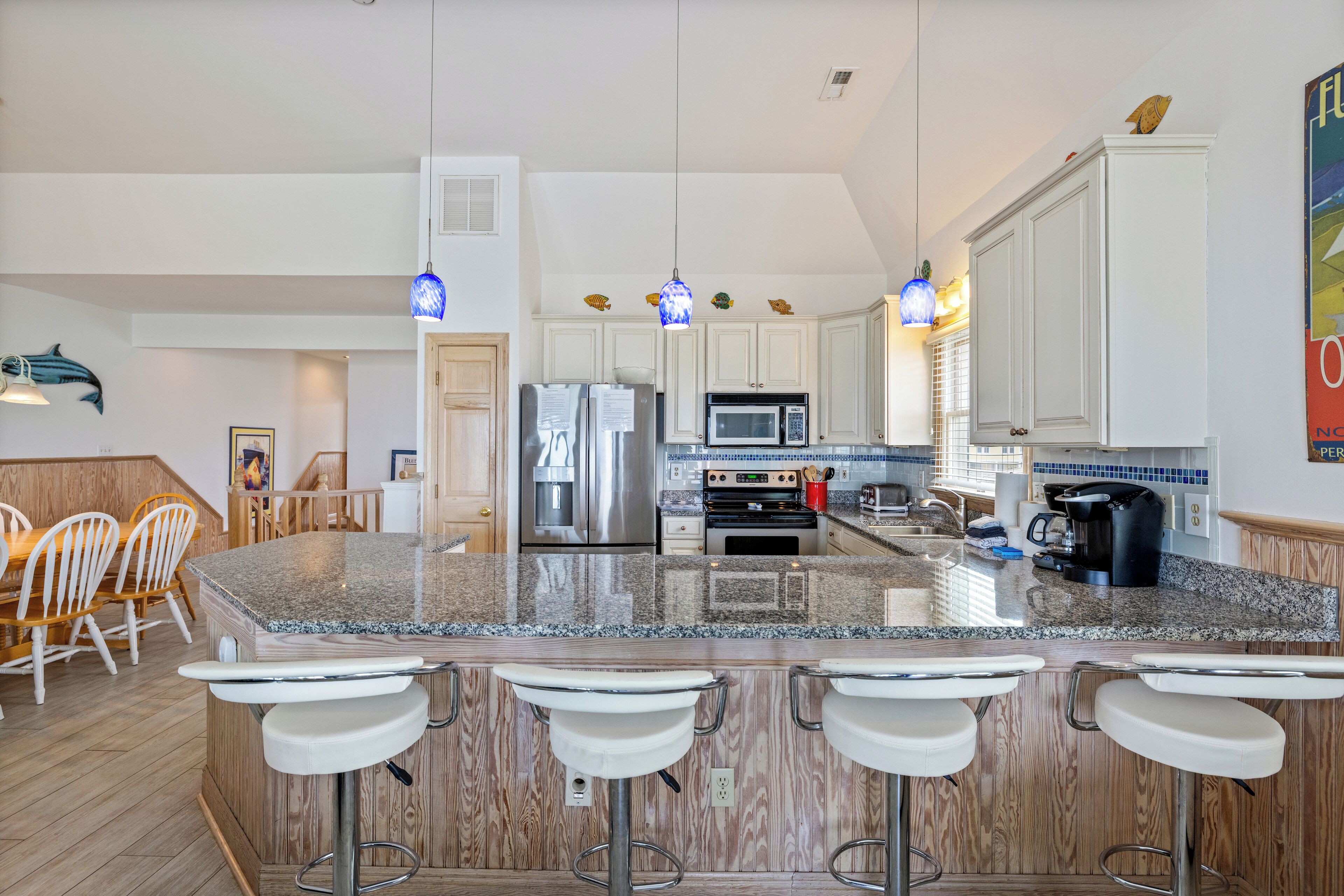A modern kitchen with granite countertops, stainless steel appliances, and bar stools.