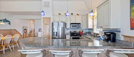 A modern kitchen with granite countertops, stainless steel appliances, and bar stools.