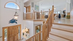 A multi-level home interior with a staircase, wooden railings, a dining area, and a view of the outdoors. - Direct Oceanfront Access*Hot Tub*Neighborhood Pool (Nags Head)