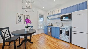 Une cuisine avec des meubles de rangement bleus, un réfrigérateur blanc, une cuisinière et une table à manger avec des chaises.