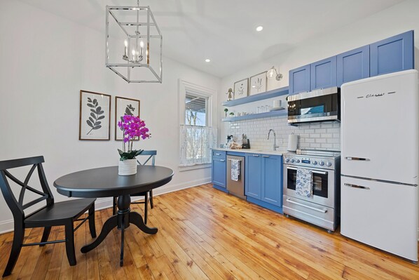 A kitchen with blue cabinets, a white refrigerator, a stove, and a dining table with chairs.