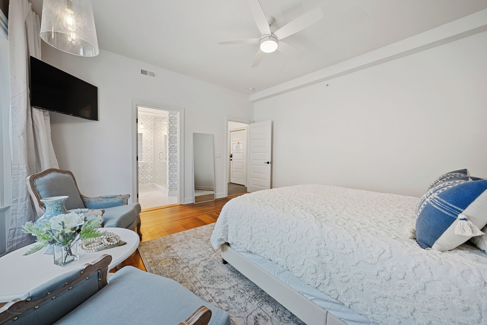 A bedroom with a bed, a desk, a chair, a television, and a ceiling fan.
