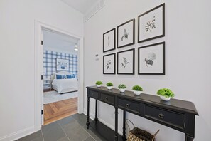 A hallway with a black console table, six framed botanical prints, and a basket on the floor.