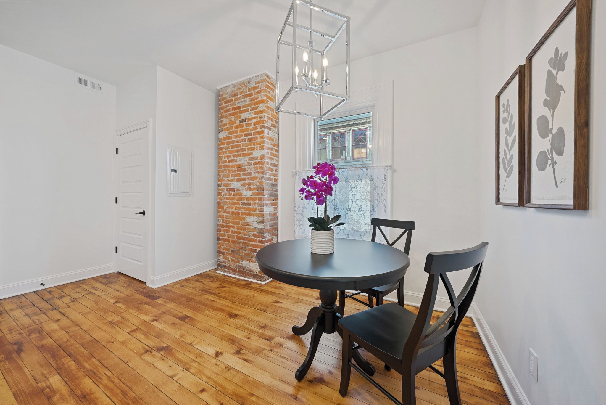 A dining area with a round table, two chairs, a potted plant, and a brick wall.