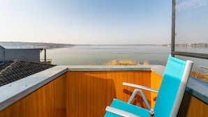 Un balcon doté d’un plancher en bois, d’une chaise bleue et offrant une vue sur une étendue d’eau paisible.