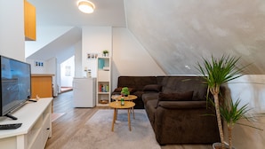 Un salon moderne avec un téléviseur à écran plat, un canapé marron, une table basse et une plante en pot.
