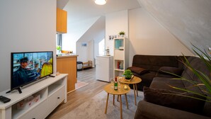 Un salon moderne avec une télévision, un canapé, une table basse et un coin cuisine à l’arrière-plan.