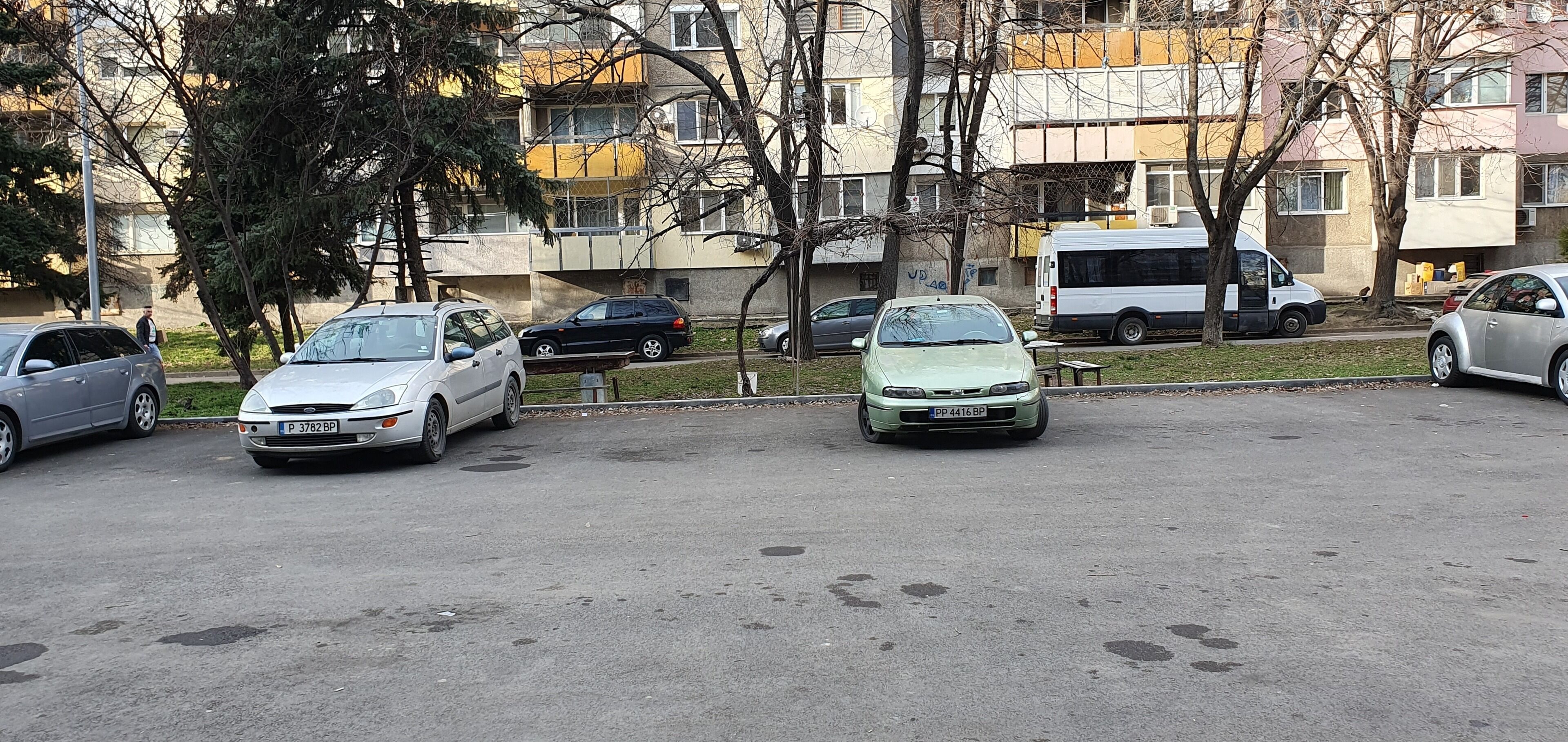 Un parking avec plusieurs voitures, un autobus et des immeubles d’habitation en arrière-plan.