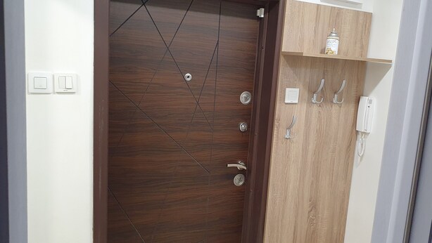 A wooden door with a modern handle, a light switch, and a wall-mounted hook. - Apartment for guests Krasy (Ruse)