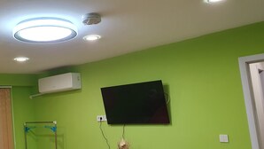 A room with green walls, a mounted flat-screen TV, an air conditioning unit, and a ceiling with recessed lighting. - Apartment for guests Krasy (Ruse)