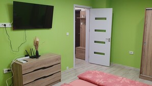 A room with a green wall, a wooden dresser, a bed with a floral bedspread, a wardrobe, and a television mounted on the wall. - Apartment for guests Krasy (Ruse)