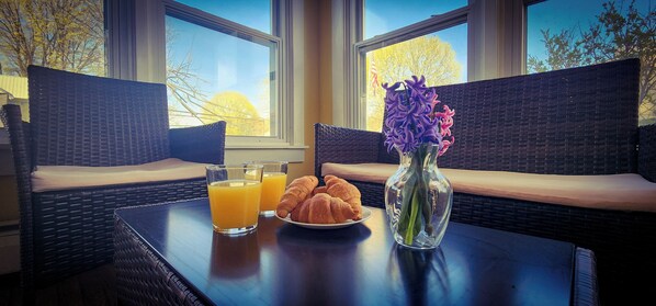 Desayuno dispuesto con mobiliario de mimbre, un jarrón de flores y croissants sobre una mesa.