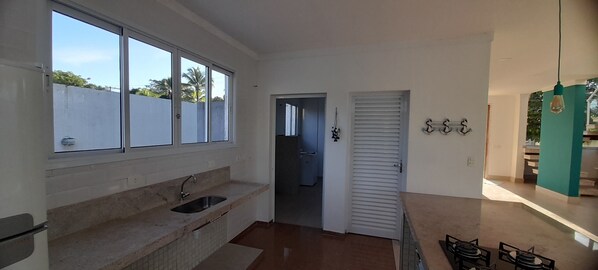 A kitchen with a large window, a sink, and a door leading to another room. - Desired Home Beachfront Residence (Morada da Praia Bertioga)