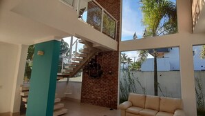 Un interno moderno con una scala, un divano e ampie finestre che offrono vista su palme e un edificio all'esterno.