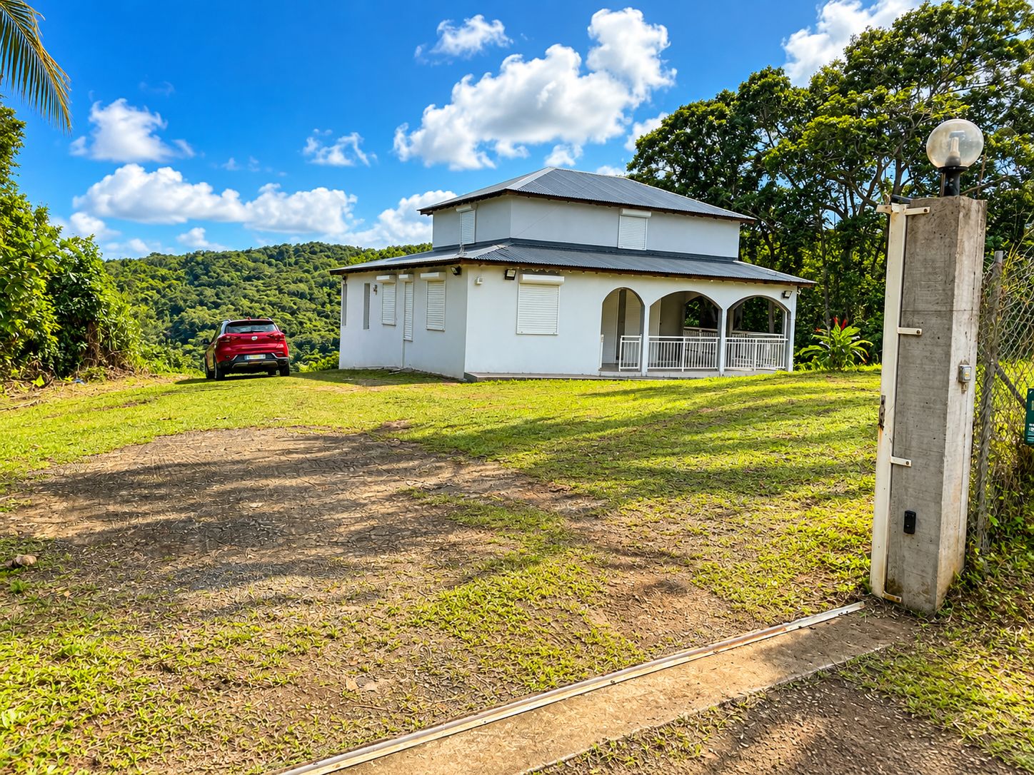 A two-story building with a porch, a red car parked in front, and a clear sky.