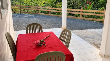 Un área de comedor exterior cubierta con una mesa dispuesta para dos personas, rodeada de sillas, y vistas a zonas verdes y colinas al fondo.