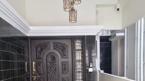 A dark brown door with intricate designs, a potted plant, and a security camera above. - lg signature stays (Bangalore)