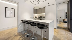 A modern kitchen with a white countertop, three black bar stools, and a large mirror. - Spacious Central Flat with Central A/C (London)
