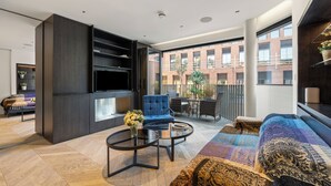A modern living room with a sofa, armchair, and coffee table. There is a TV mounted on the wall, and a balcony with a view of buildings. - Spacious Central Flat with Central A/C (London)
