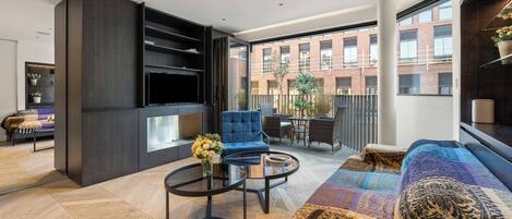 Un salon moderne avec un canapé, un fauteuil et une table basse. Un téléviseur est fixé au mur, et un balcon offre une vue sur les immeubles.