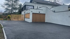 Ein modernes, zweigeschossiges Haus mit Garage, Holzzaun und gepflasterter Auffahrt.