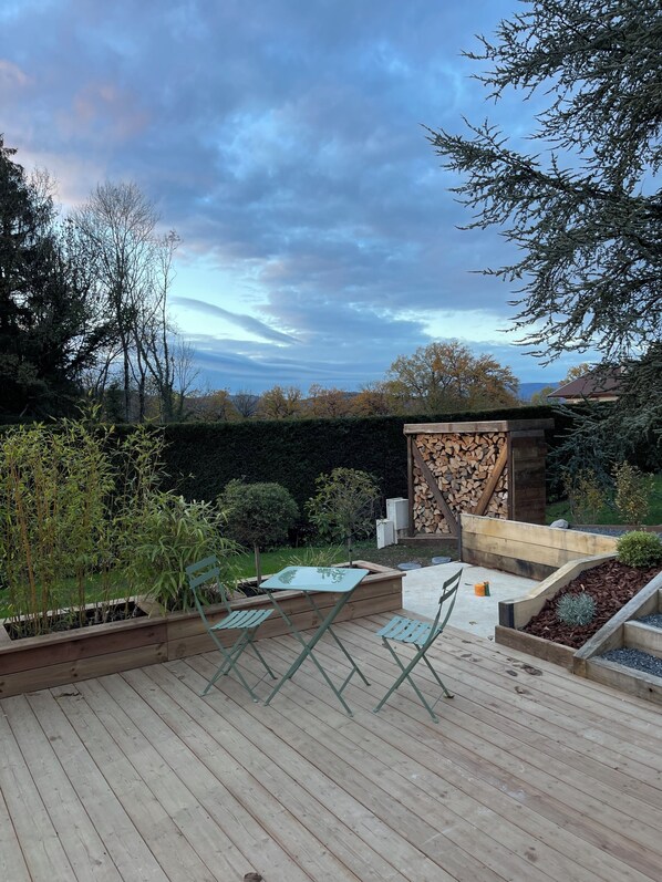Un patio in legno con tavolo e sedie, circondato da piante e un muro in pietra.