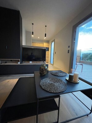 Una cucina moderna con un grande televisore, mobili in legno e un'area pranzo con un tavolo nero e due sottopiatti in fibra naturale.