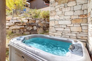 A hot tub with a stone wall backdrop, surrounded by a stone wall and vegetation.
