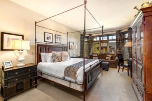 A four-poster canopy bed with a wooden headboard, a nightstand with a lamp, a sofa, and a cabinet with a mirror.