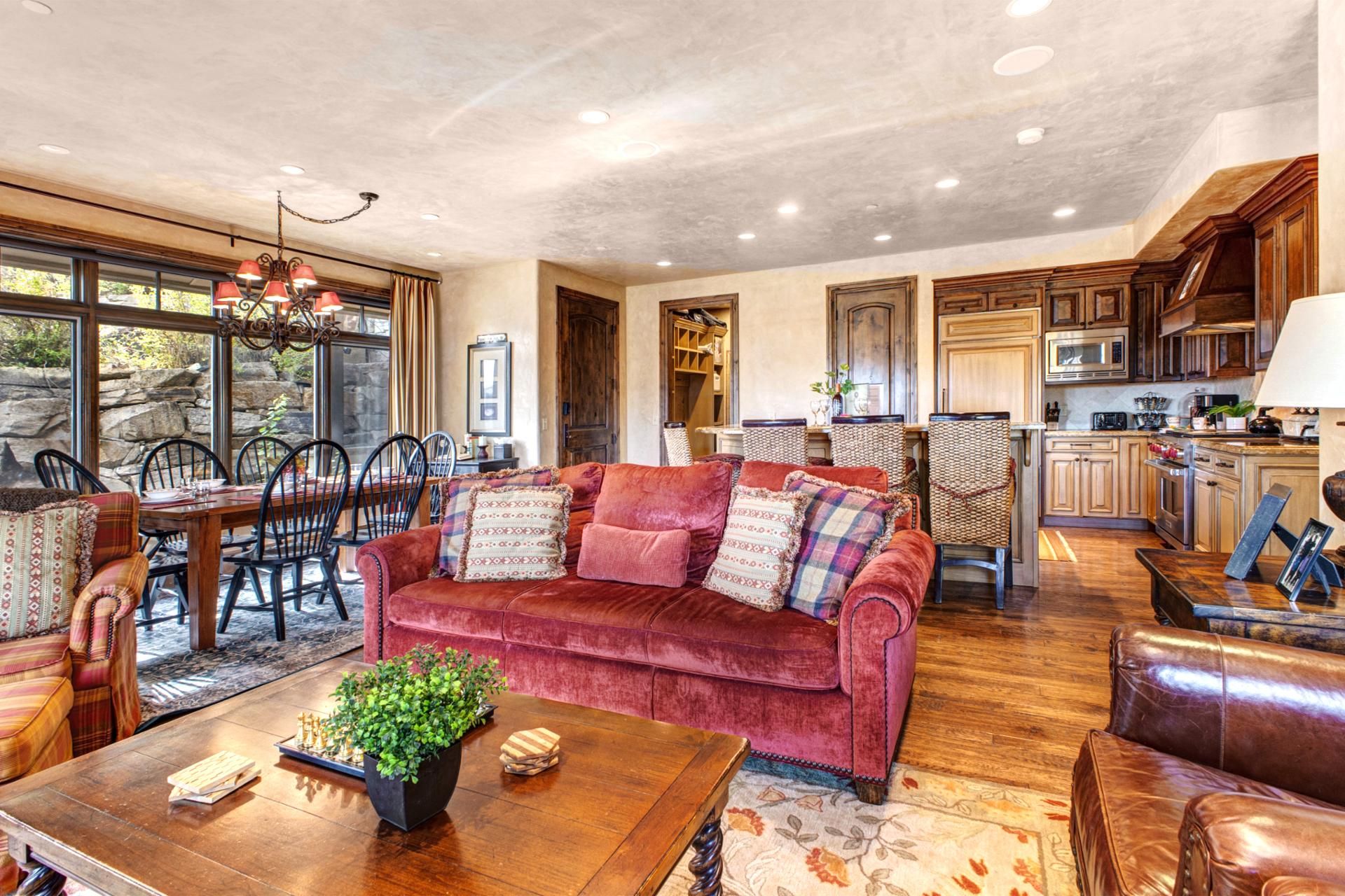 A spacious living area with a red velvet sofa, wooden dining table, and chairs.