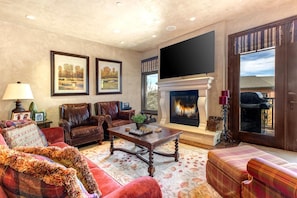 A living room with leather sofas, a fireplace, a flat-screen TV, and framed landscape paintings.