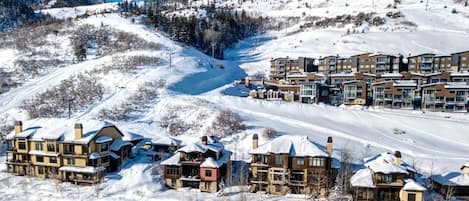 Estância de esqui nas montanhas coberta de neve, com edifícios altos, pistas e céu azul límpido.