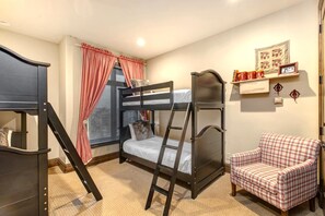 Une chambre avec un lit superposé, une échelle, un fauteuil à carreaux et une fenêtre avec des rideaux.