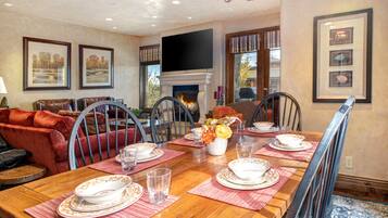 A dining room with a wooden table set for four, a fireplace, and framed artwork on the walls.