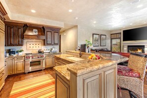 A spacious kitchen with a large island, wooden cabinets, and a built-in oven. There is a dining area with a sofa and a fireplace.