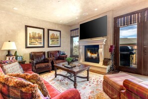 A spacious living room with leather sofas, a fireplace, and a large TV mounted on the wall.