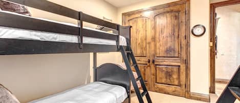 A bunk bed room with a ladder, a wooden door, and a wall clock.